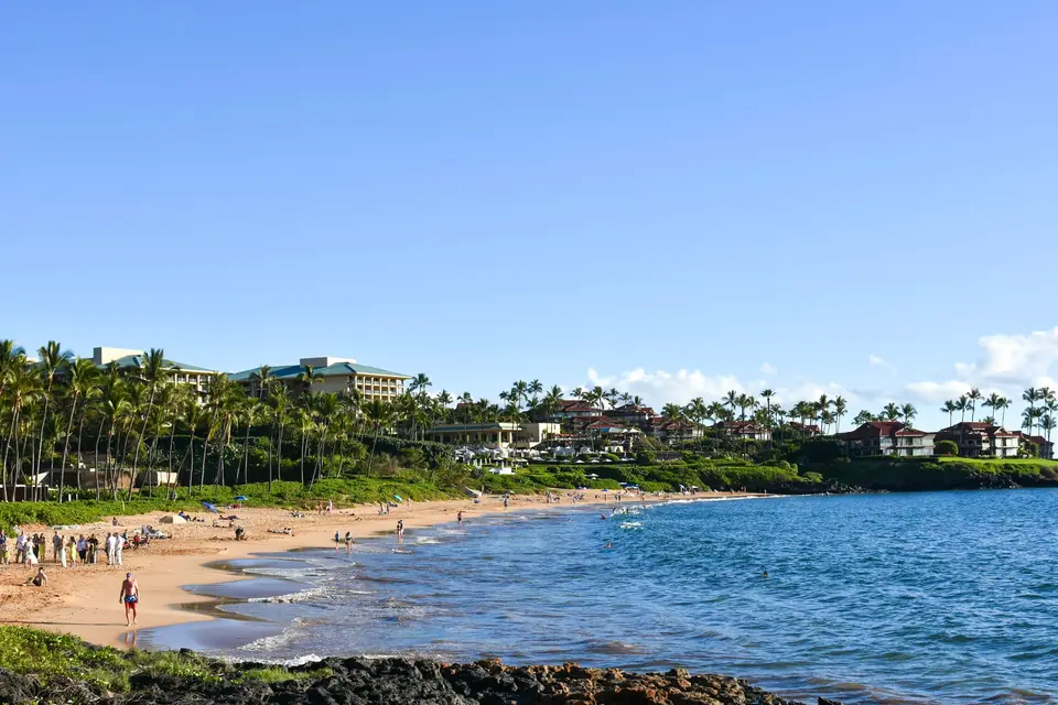 a group of people walking along a beach next to the ocean — Maui