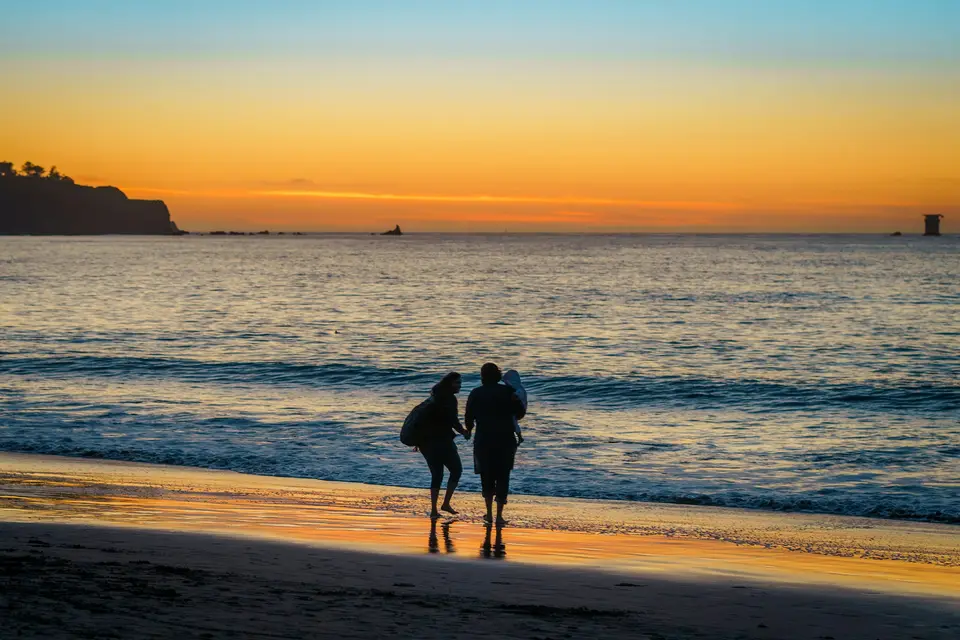 a couple of people walk on the beach with surfboards — San Francisco