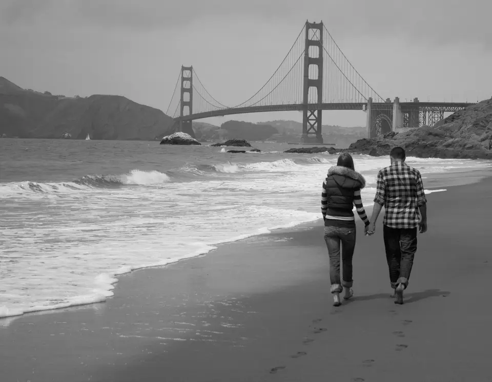 grayscale photography of man and woman walking near seashore viewing Golden Gate bridge — San Francisco