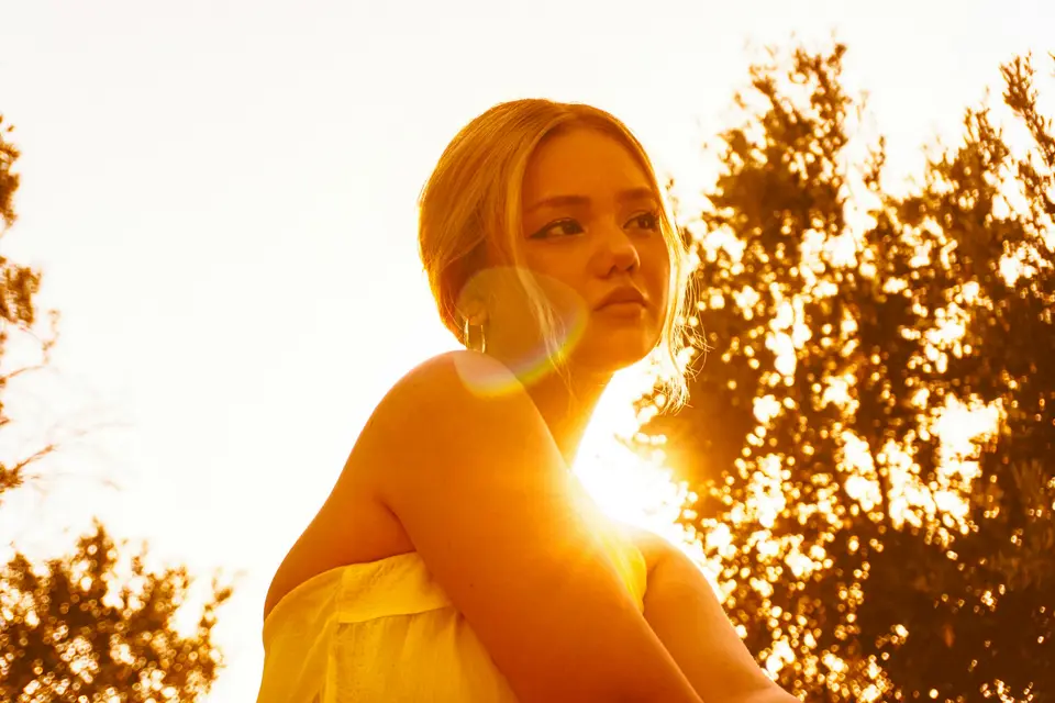 A woman in a yellow top backlit by low golden light outdoors
