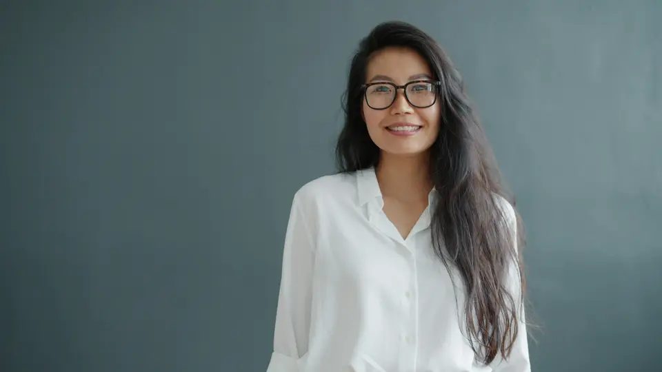 A woman with glasses smiles against a gray background